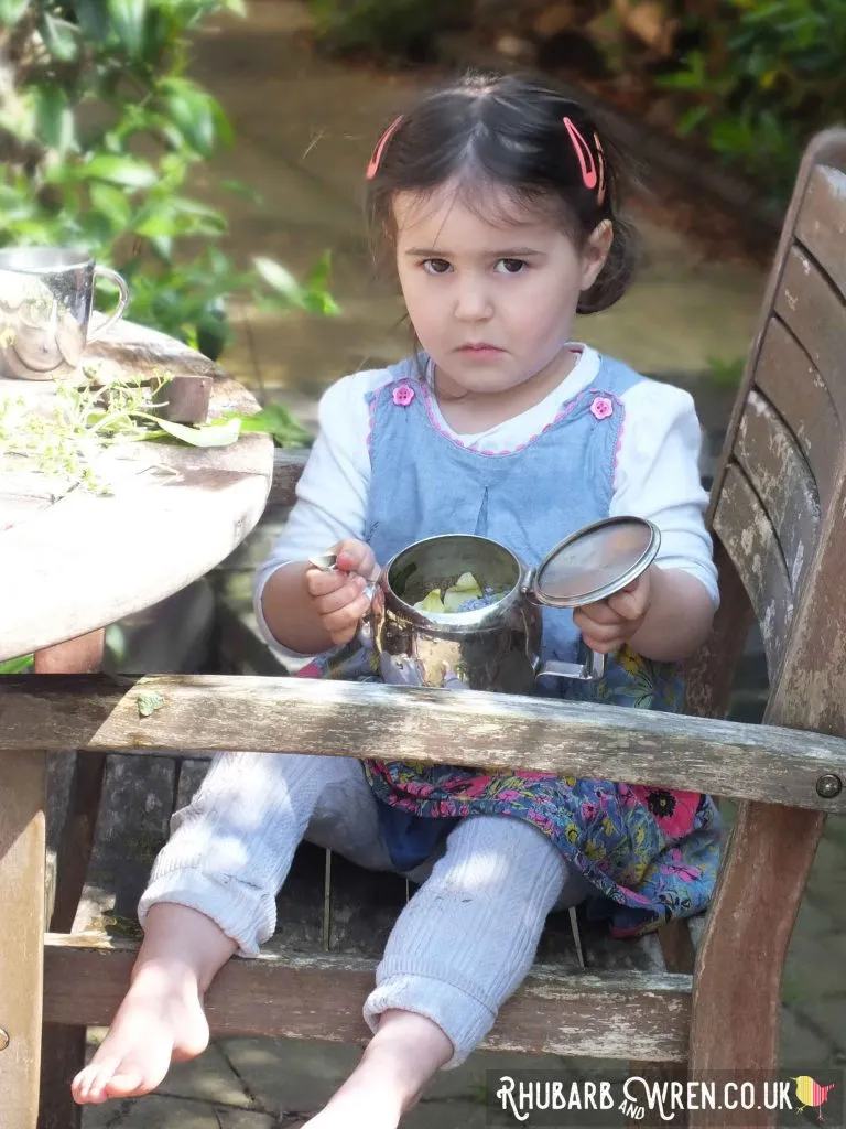child looking in empty teapot in garden
