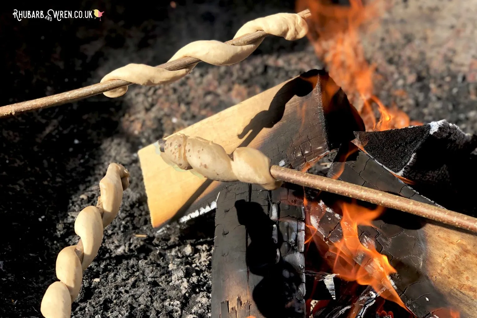 Twists of cinnamon damper bread being cooked over a fire on sticks.