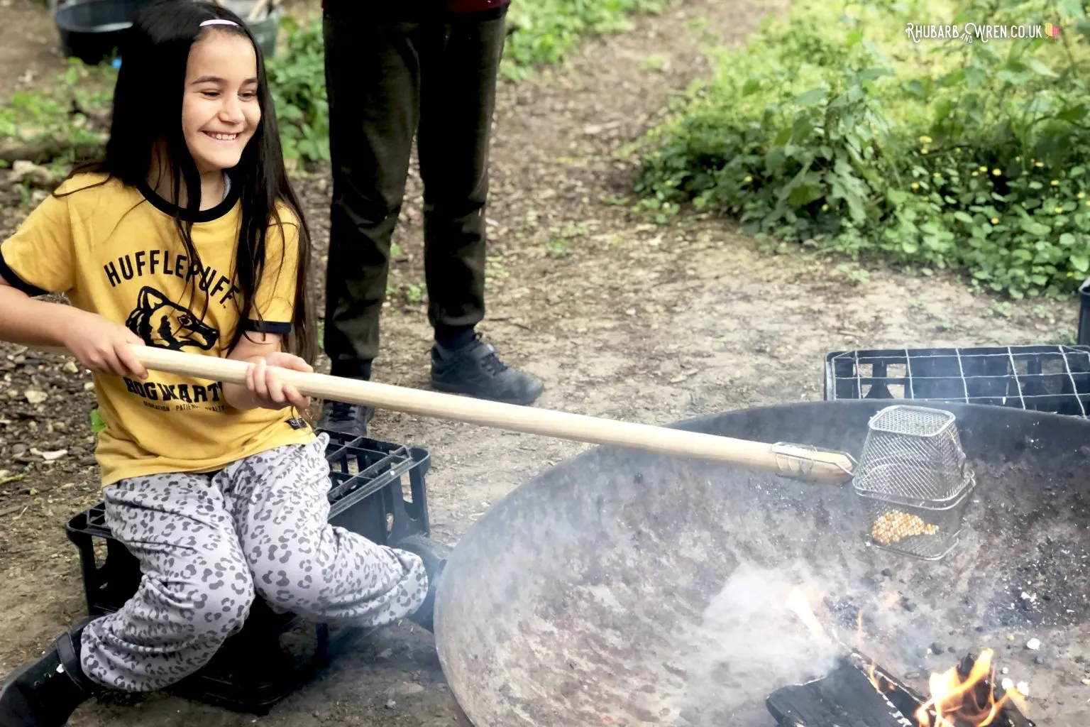 Girl cooking popcorn over a campfire using a cage on a stick